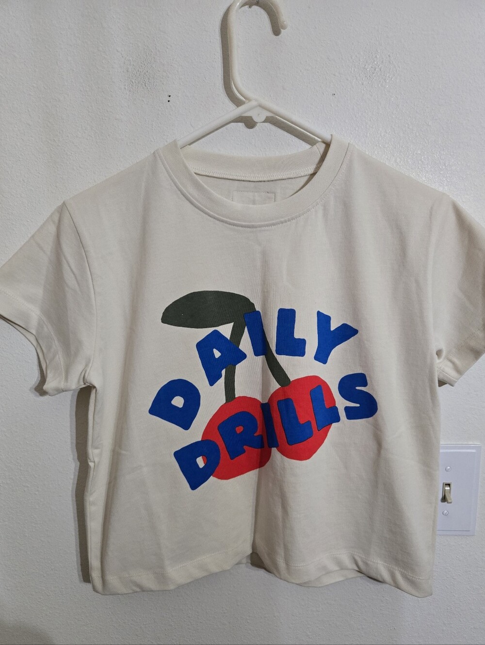 Daily Drills Cream Tee with Red Cherry Graphic and Blue Lettering